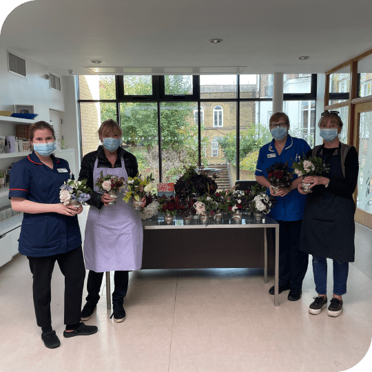 2 nurses and 2 women standing in front of a table holding donated flower arrangements