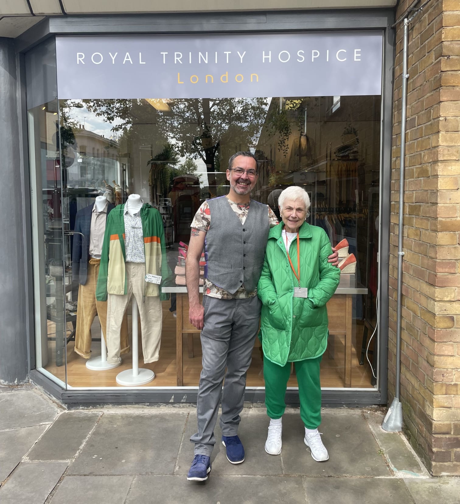 Man in a suit and woman in an all green outfit stood in front of a Trinity shop