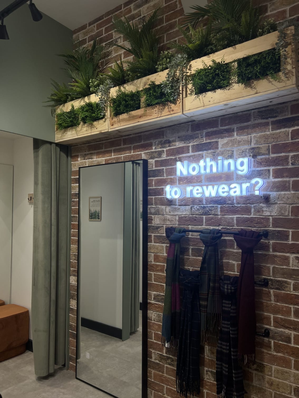 a brick wall with nothing to wear in neon, and a mirror and planters