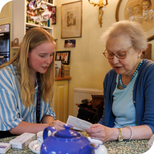 An older woman and a younger woman sat looking at a piece of paper 