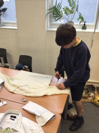 A year 6 child cutting the sleeves off a jumper