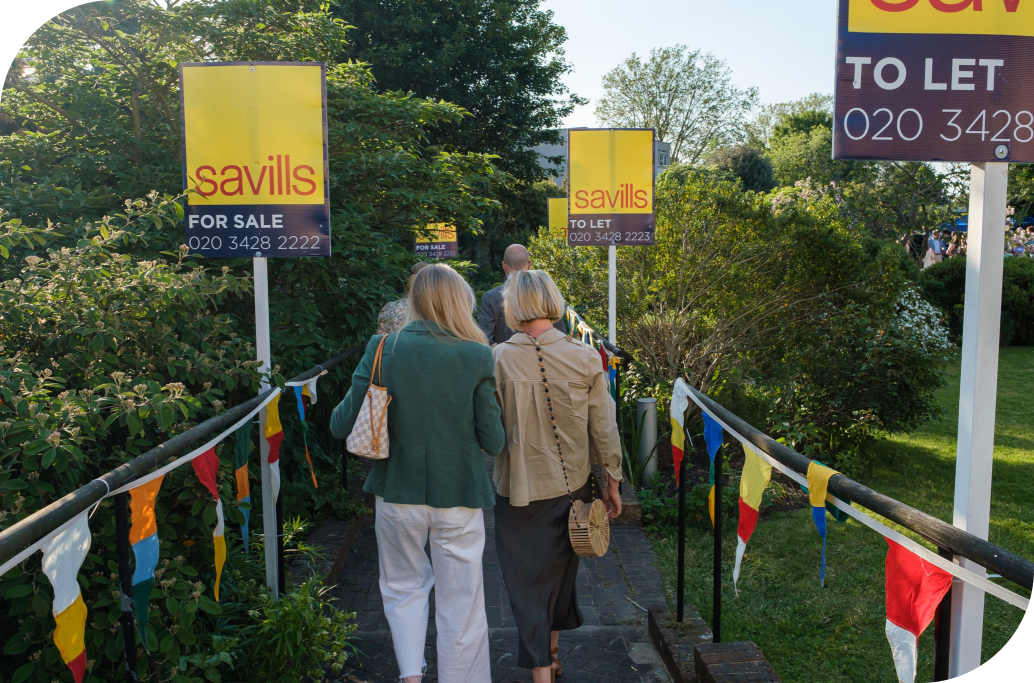 2 women walking down a path with Savills bright yellow signs on either side