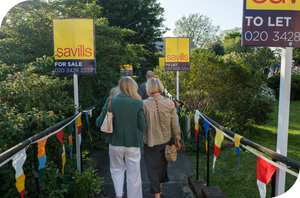 2 women walking down a path with Savills bright yellow signs on either side