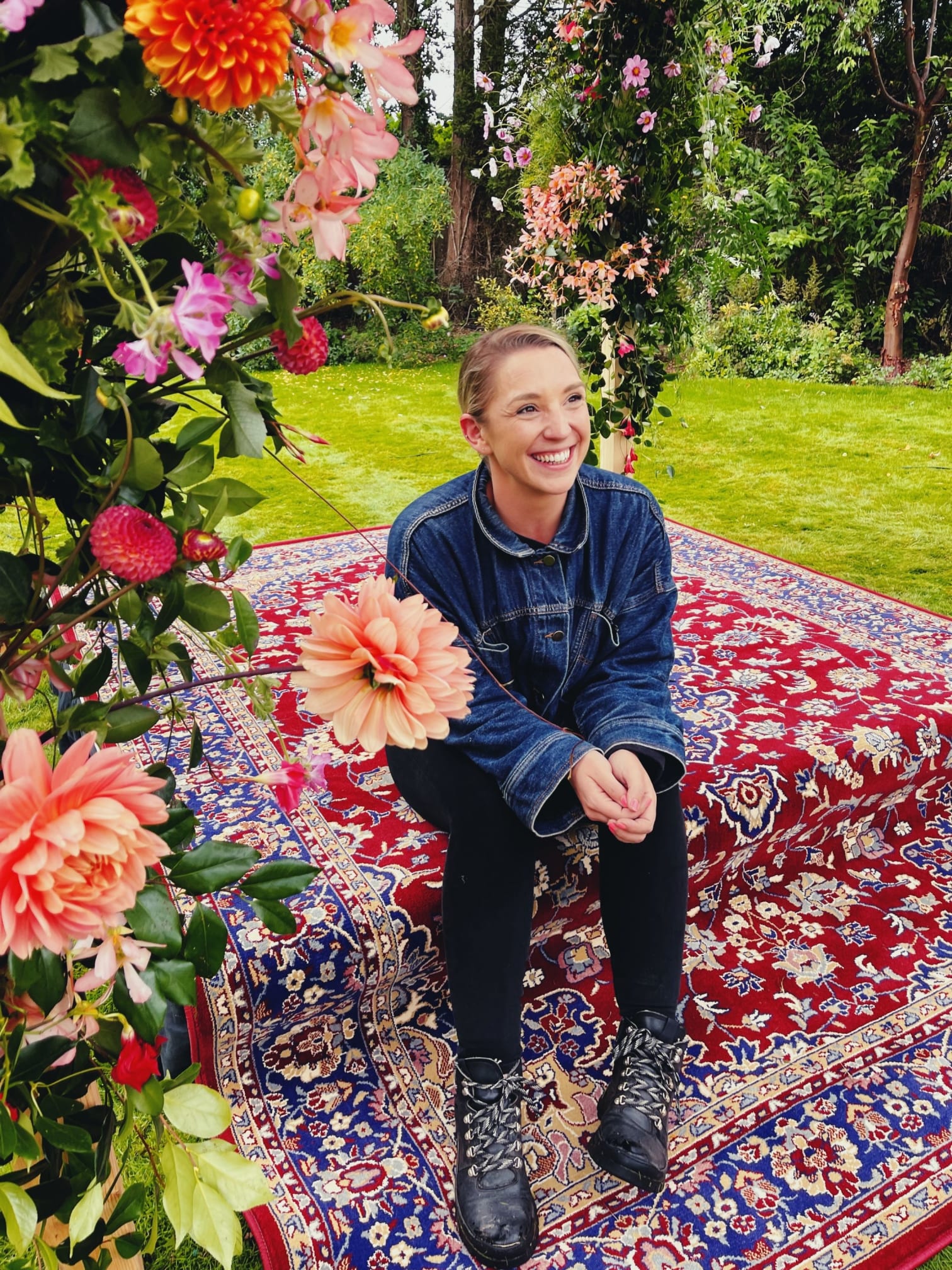 Woman sitting on a patterned rug in a garden with peach flowers in the photo