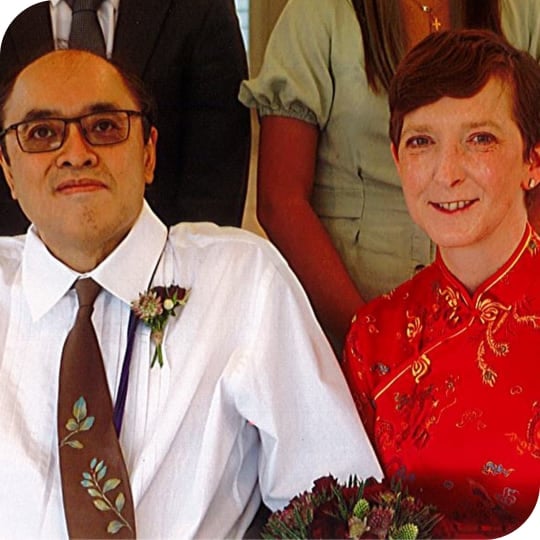 A man wearing a shirt and brown tie and a women wearing a red Asian-inspired dress